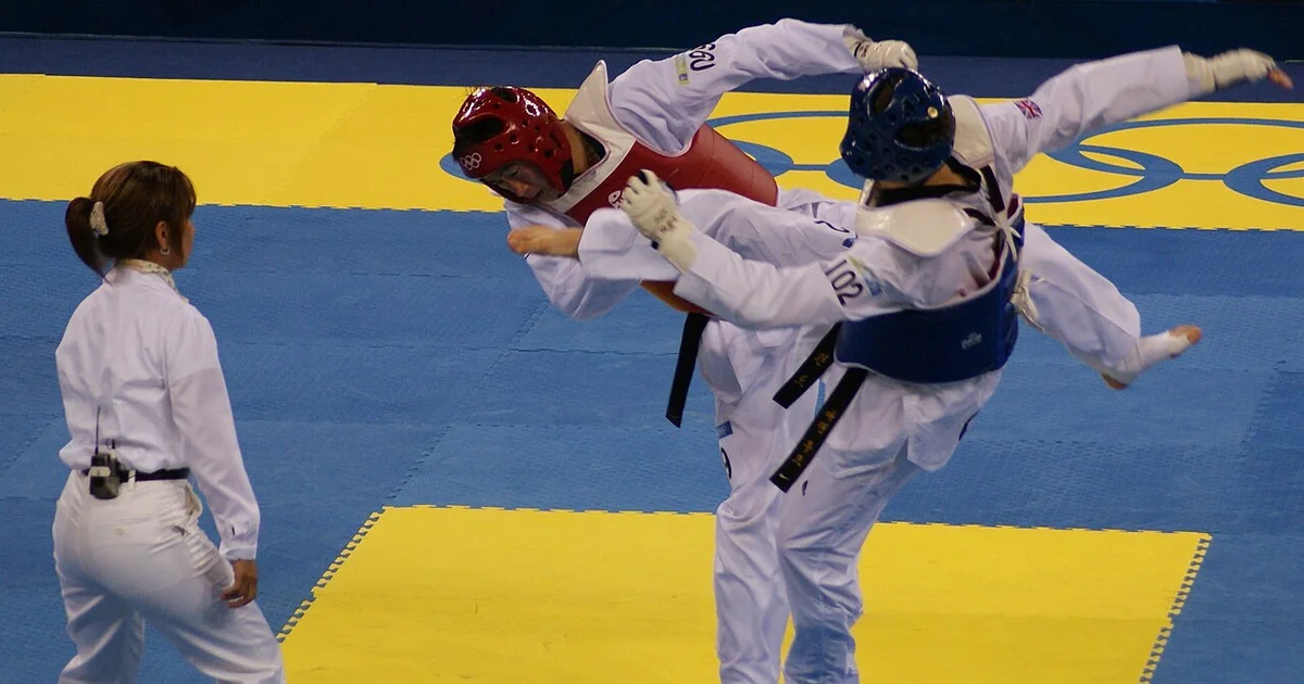 Comparación de karate vs taekwondo — practicante de karate en postura de combate junto a practicante de taekwondo en postura de pateo con peso adelantado. La diferencia de posturas por sí sola codifica las divergentes prioridades tácticas de las dos artes.