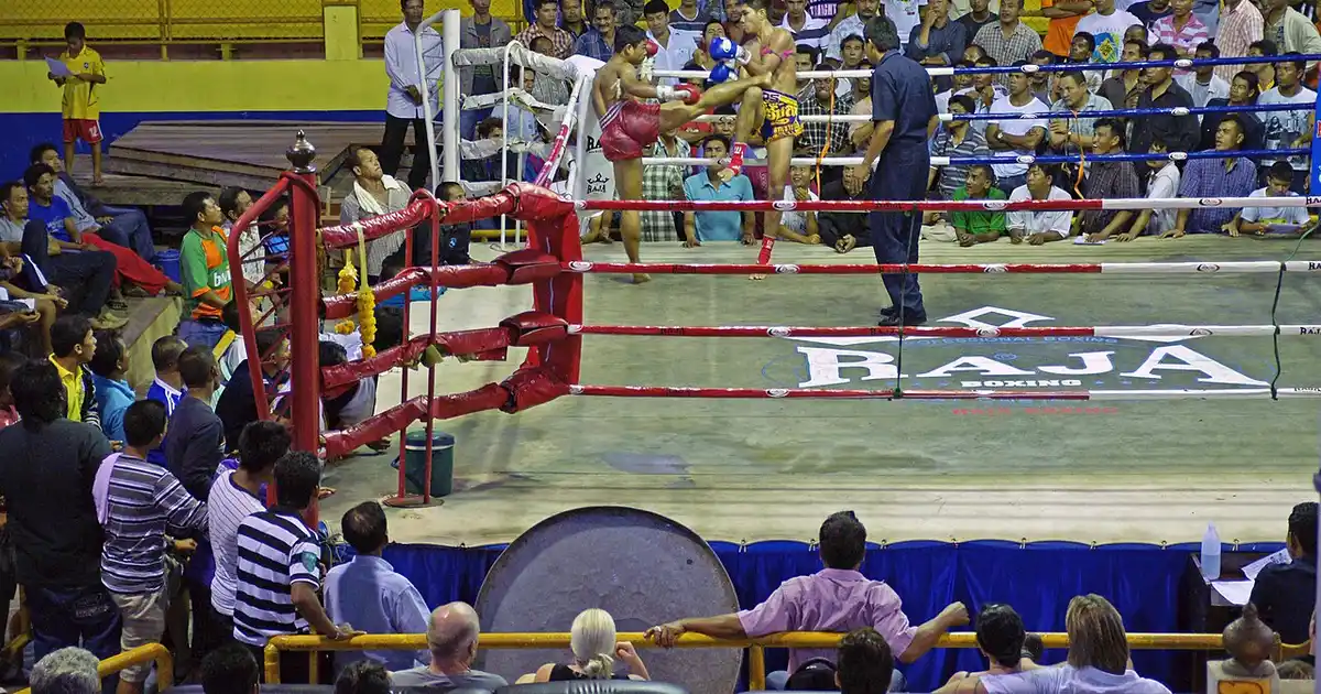 Entrenamiento de Muay Thai — un peleador practicando una patada circular (roundhouse kick) en pads thai en un gimnasio de Bangkok