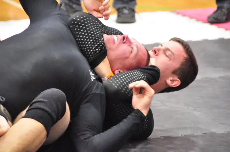 A submission grappler applying a rear naked choke during no-gi competition — back control with hooks in, arm under the chin. CC BY 2.0 via Wikimedia Commons