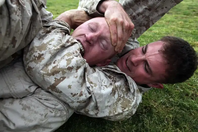 A US Marine applying a rear naked choke during MCMAP (Marine Corps Martial Arts Program) grappling training — the choking arm is under the chin, across the front of the throat, compressing both carotid arteries. Public domain, US Marine Corps via Wikimedia Commons