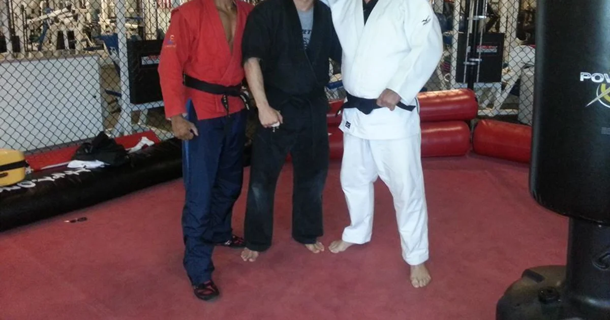 Sambo and judo athletes gripping up in competition — sambo's kurtka jacket and shorts versus judo's full gi illustrate the divergence of two arts that share a common ancestor in Kodokan judo.