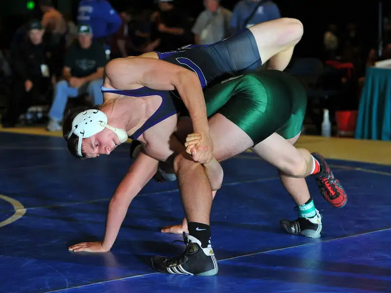 A wrestler applying a spladle during a folkstyle wrestling match — the attacker controls the head while splitting the opponent's legs apart. CC BY-SA 2.0 by Chris Hunkeler via Flickr