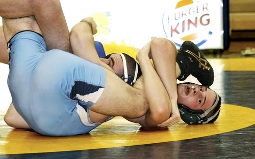 A wrestler caught in a spladle pin position on the mat — the legs are being forced apart while the upper body is controlled. Public domain via Flickr